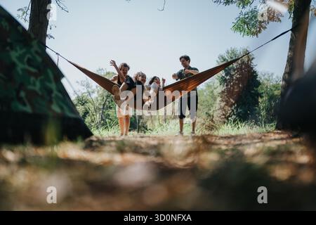 Freunde und Familie entspannen sich in einer Hängematte beim Camping im Freien unter sonnigem Himmel Stockfoto