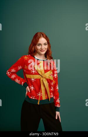 Eine fröhliche junge Rothaarige posiert an einem Wintertag in einem fröhlichen Weihnachtspullover. Stockfoto