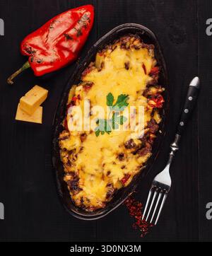 Moussaka mit geschmolzenem Käse, dekoriert mit Petersilie, Backen und Bubbeln in einer Pfanne, mit einer Gabel und gegrilltem Pfeffer an der Seite Stockfoto