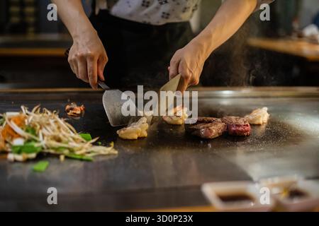 Teppanyaki, japanische Teppanshow in traditionellem Restaurant. Hände des Kochs. Der Koch bereitet Fleisch, Fisch, Reis und Gemüse auf einem heißen Tisch vor den Gästen zu. Küche Völker der Welt Konzept Stockfoto