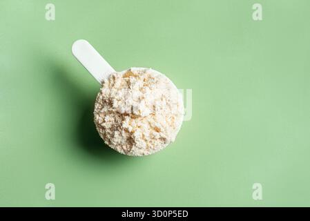 Löffel Molkenproteinpulver auf grünem Hintergrund, Nahaufnahme, Kopierraum. Stockfoto
