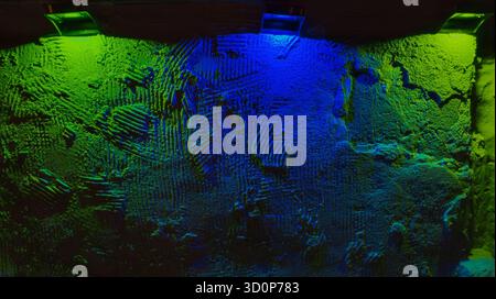 Raue Putzwand beleuchtet von grünen und blauen Scheinwerfern, schwere Textur und stimmungsvolle Farben schaffen dramatische abstrakte Kulisse Stockfoto