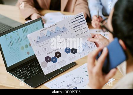 Junge Erwachsene asiatische Frau analysiert Finanzdiagramme während des Gesprächs auf dem Smartphone Stockfoto