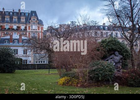 Ein Park mit einer weißen Marmorstatue im Vordergrund, umgeben von blattlosen Bäumen und Bänken, mit klassischen Gebäuden im Hintergrund. Stockfoto