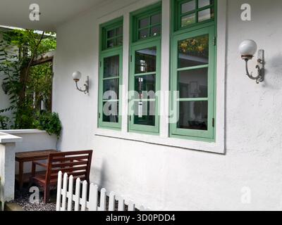 Ein kleiner Eckbereich mit einer Holzbank und einem Tisch neben alten, mintgrün gerahmten Fenstern Stockfoto