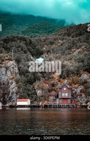 Eine Angelhütte am Flussufer, umgeben von hohen Klippen, die mit Wald bedeckt sind. Nebel hat sich auf den Berggipfeln angesiedelt. Stockfoto