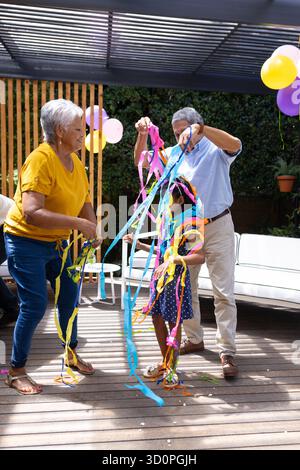 Großeltern und Kind spielen auf einer Familienparty im Freien mit farbenfrohen Luftschlangen. Feiern, generationenübergreifend, draußen, Bindung, Glück, Sommerzeit || Modell veröffentlicht Stockfoto