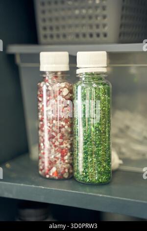 Farbenfrohe Perlenbehälter mit roten und grünen Perlen in durchsichtigen Kunststoffflaschen im Regal. Stockfoto