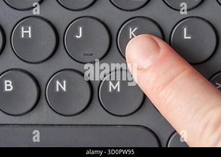 Nahaufnahme des Fingers, der die Taste k auf der schwarzen Tastatur mit kreisförmigen Tasten drückt. Stockfoto