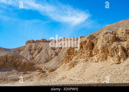 Aus nächster Nähe sehen Sie die steilen, kargen Felswände und die sonnenüberfluteten Berge des Tals der Könige in Luxor, Ägypten, vor einem tiefblauen Himmel mit schimmernden Wolken. Stockfoto