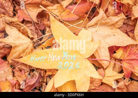 Happy New Year 2026 auf gelbem Ahornblatt geschrieben – Herbstgrußkonzept. Künstlerisches Foto eines gelben Ahornblattes mit Text Happy New Year Stockfoto