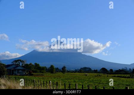Malerische Ausblicke auf Mount Taranaki (Mount Egmont) in der Nähe von New Plymouth, Neuseeland, mit ländlichen Landschaften, Straßen und üppigem Grün unter blauem Himmel. Stockfoto