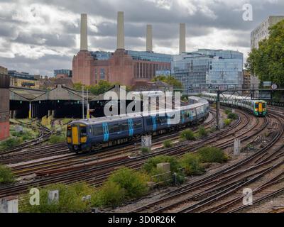 Die Züge verkehren auf Gleisen von und zum Bahnhof Victoria an einer stark frequentierten Eisenbahnkreuzung, wobei das Battersea Power Station im Hintergrund in London, Großbritannien, sichtbar ist Stockfoto