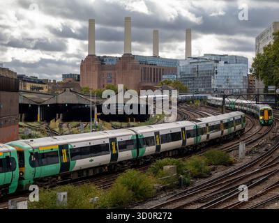 Die Züge verkehren auf Gleisen von und zum Bahnhof Victoria an einer stark frequentierten Eisenbahnkreuzung, wobei das Battersea Power Station im Hintergrund in London, Großbritannien, sichtbar ist Stockfoto