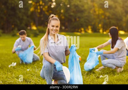 Müll aufsammeln, grünen Park reinigen, Gruppenfreunde arbeiten, blaue Handschuhe tragen, Taschen Stockfoto