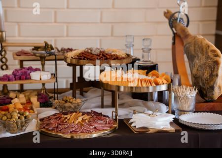 Ein einladender Wurstaufstrich mit Wurstwaren, Käse, Oliven und einem markanten Schinkenschwein, der auf Ständen vor einer weißen Ziegelwand angeordnet ist Stockfoto