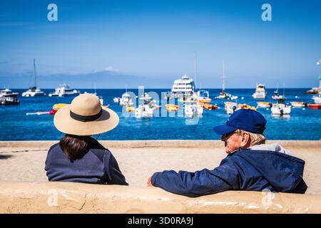 Avalon, Catalina Island, CA USA - 25. April 2019: Paare sitzen auf einer Bank und genießen den Meerblick am Avalon Harbor. Stockfoto