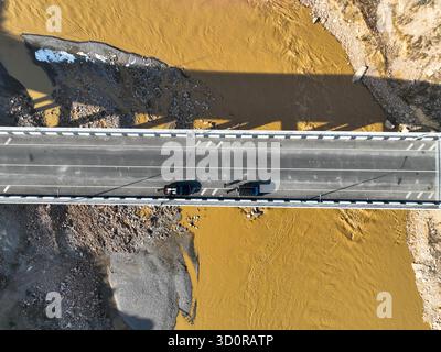 Bischkek, Kirgisistan - 13. Oktober 2024: Strenger Blick von oben nach unten auf zwei Fahrzeuge, die eine moderne Brücke überqueren, die eine breite, silbrige, gelblich-braune Brücke überspannt Stockfoto