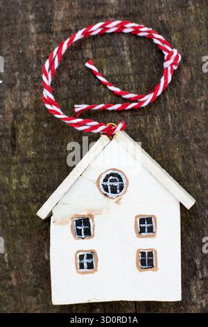 Ein bezauberndes weißes hölzernes Haus-Ornament mit rot-weißem Garn auf einer rustikalen Holzoberfläche, das an eine gemütliche, handgefertigte Ästhetik erinnert. Stockfoto