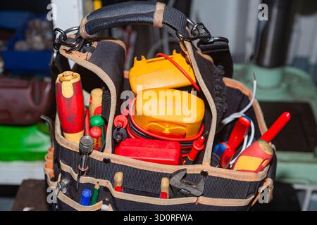 In der Werkstatt steht eine Elektrikertasche voller Werkzeuge Stockfoto