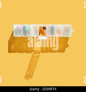 Wöchentlicher Pillen-Organisator mit Schatten auf gelbem Hintergrund mit verschiedenen bunten Tabletten. Stockfoto