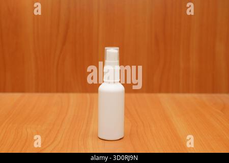 Eine saubere weiße Sprühflasche steht aufrecht auf einem Holztisch. Der Hintergrund ist schlicht und glatt und hebt die Flasche hervor. Stockfoto