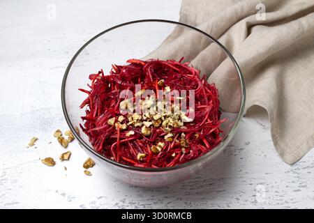 Gesunder Rote-Bete-Salat mit gehackter Karotte, Sellerie, Zwiebeln und gehackten Walnüssen in einer Glasschale auf hellem texturiertem Hintergrund. Frisches vegetarisches Gericht Stockfoto