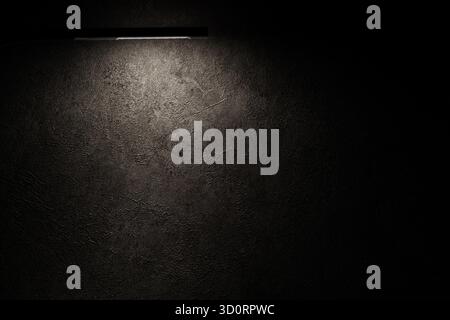 Eine lineare Leuchte wirft ein weiches Licht auf eine dunkle Wand. Minimaler Werbehintergrund mit Platz für Text oder Logo. Stockfoto