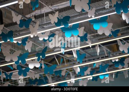 Eine künstlerische Deckeninstallation mit einer lebendigen Ausstellung von weißen und blauen Papierschmetterlingen, die eine moderne, dekorative und skurrile Atmosphäre schafft Stockfoto