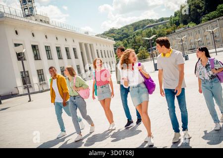 Gruppe von verschiedenen jungen Freunden, die an einem sonnigen Tag in einer urbanen Umgebung mit Rucksäcken im Freien spazieren Stockfoto