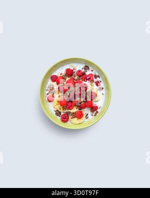 Bunte Frühstücksschale mit Banane, Himbeere, Schokolade und Joghurt auf hellem Hintergrund, die gesunde Ernährung und Morgenenergie symbolisiert Stockfoto