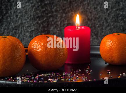 Mandarinen und rote Kerze auf dunklem Hintergrund - Weihnachtsfesttagstisch mit Mandarinen Stockfoto