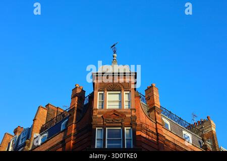 Historisches rotes Backsteingebäude mit kunstvoller Architektur und Schornsteinen unter einem klaren blauen Himmel im Zentrum von London Stockfoto