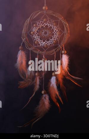 Wunderschöner Traumfänger, der in farbigen Lichtern vor dunklem Hintergrund mit Rauch hängt Stockfoto