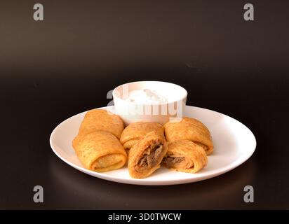 Frische Pfannkuchen gefüllt mit Hackfleisch und einer Tasse Sauerrahm auf einem runden Teller auf schwarzem Hintergrund. Nahaufnahme. Stockfoto