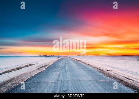 Eisbedeckte offene Slippy Road am Winterabend. Sonnenuntergang Sonnenaufgang Himmel. Gefährliche Bewegung. Frosted Asphalt Country Open Road Durch Winter Schnee Stockfoto