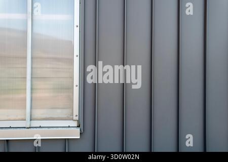 Das Detail einer Wellblechverkleidung und eines Abschnitts eines Fensterrahmens an einer Außenwand Stockfoto