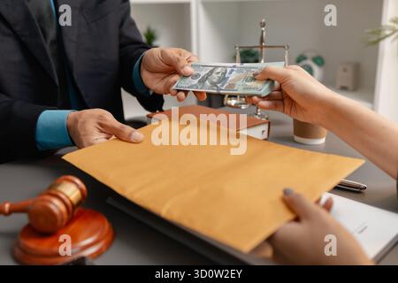 Ein Kunde übergibt einem Anwalt einen Stapel Bargeld, der einen braunen Umschlag auf dem Schreibtisch hält, der Bestechung, Korruption und unethische finanzielle Geschäfte symbolisiert Stockfoto