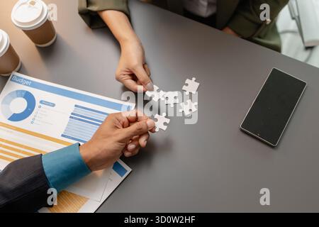 Geschäftsleute halten Puzzleteile auf dem Schreibtisch zusammen und symbolisieren Teamarbeit, Zusammenarbeit, Planung und Strategieentwicklung für Effektivität Stockfoto