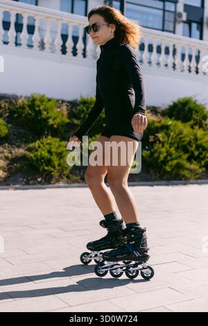 Sportliche junge Frau, die im Freien in schwarzer Sportbekleidung, aktivem Lebensstil und Fitness unterwegs ist Stockfoto