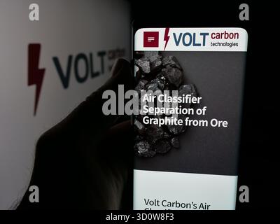 In dieser Abbildung hält eine Person ein Handy mit der Webseite des kanadischen Unternehmens Volt Carbon Technologies Inc. Vor dem Logo. Stockfoto