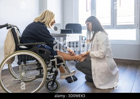 Arzt untersucht Bein und Knöchel eines Patienten, der Patient sitzt im Rollstuhl während einer Sprechstunde zur Physiotherapie oder Rehabilitation in einer clin Stockfoto