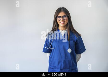 Weibliche Ärztin in blauen Peelings mit Stethoskop, selbstbewusst in die Kamera auf weißem Hintergrund lächelnd, professionelle, freundliche Gesundheitsdienstleister vertreten Stockfoto