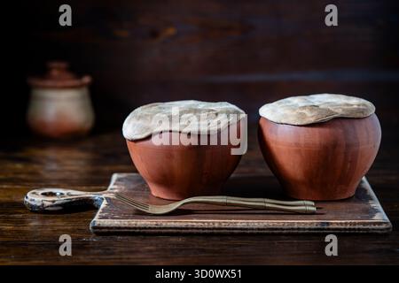 Zwei Tontöpfe mit gedünstetem Gemüse auf einem Holztisch, Nahaufnahme. Das Dünsten von Lebensmitteln in Steingut gilt als gesund Stockfoto