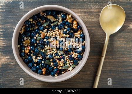 Hausgemachter grüner Buchweizen aus biologischem Anbau mit Heidelbeeren, Walnüssen, Kürbiskernen und Honig in einer Keramikschale auf hölzernem Hintergrund. Gesunde vegetarische Pause Stockfoto