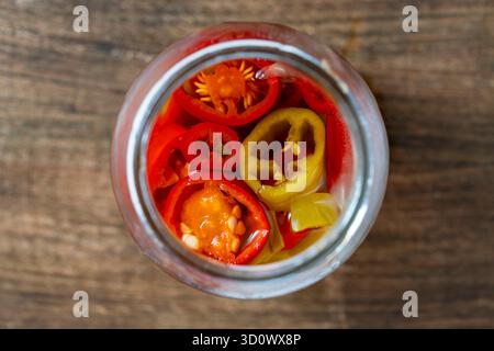 Rote und grüne Paprika mit Essig in Glasgefäß auf einem Holztisch, Nahaufnahme, Blick von oben Stockfoto