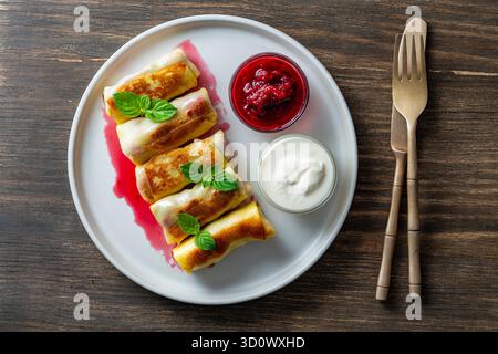 Gebratene, gerollte Pfannkuchen gefüllt mit Hüttenkäse und Kirsche, süßes Dessert auf Teller, Nahaufnahme, Blick von oben. Hausgemachtes Backen. Köstliches Fast Food für bre Stockfoto