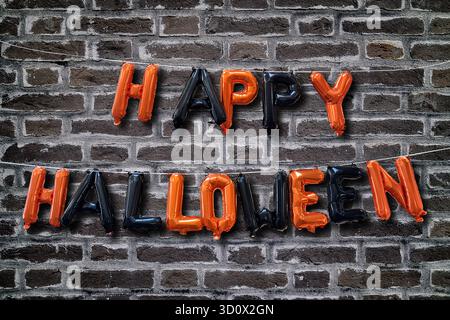 Happy Halloween, bestehend aus schwarzen und orangen Ballons vor einer dunkelgrauen Ziegelwand. Stockfoto