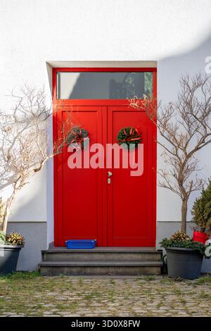 Die rote Eingangstür des Hauses ist mit zwei echten Tannenkränzen und roten Bändern verziert. Stockfoto