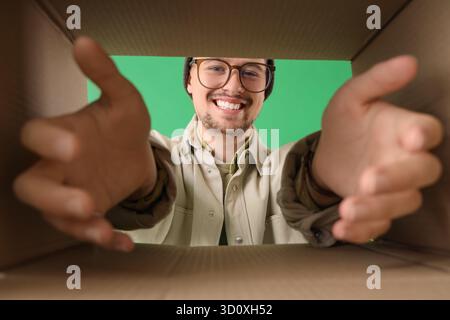 Schöner Mann mit offenem Karton auf grünem Hintergrund, Blick von innen Stockfoto